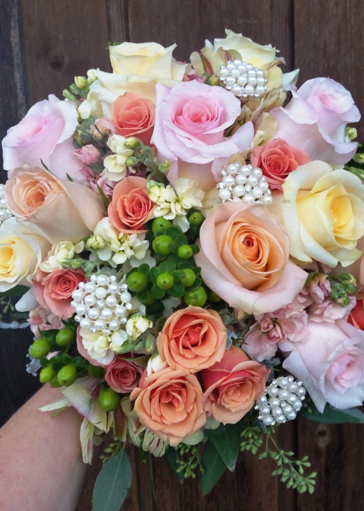 A romantic bouquet of roses in a blend of pastel colors is adorned with clusters of pearls.